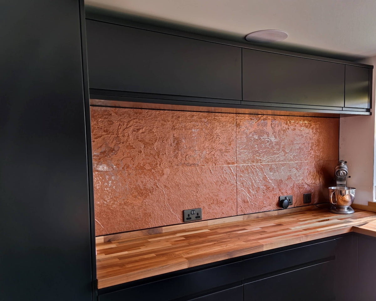 Copper metal veneer kitchen splashback with dark cabinetry and wood worktop